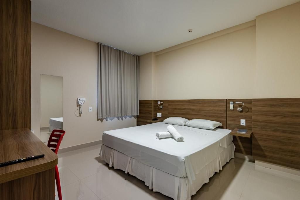 Une chambre d’hôtel avec un lit, un bureau, une chaise, un miroir et une fenêtre avec des rideaux.