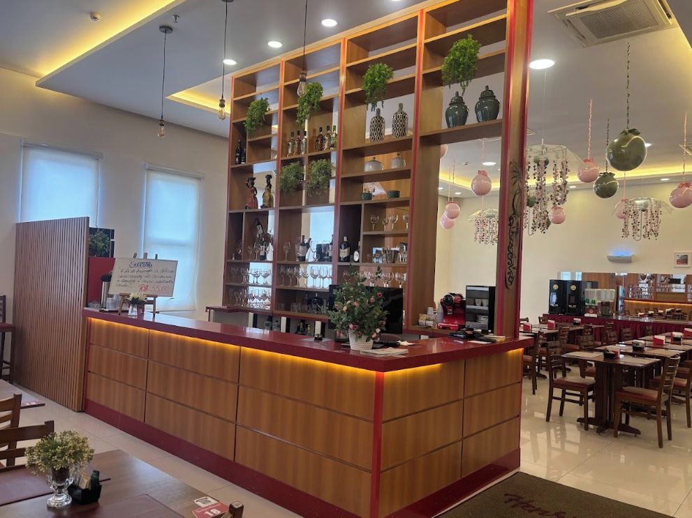 A hotel lobby with a reception desk, wooden shelving with decorative items, and a dining area with tables and chairs.