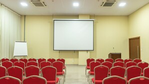 Een vergaderzaal met rijen rode stoelen, een whiteboard en een projectorscherm.