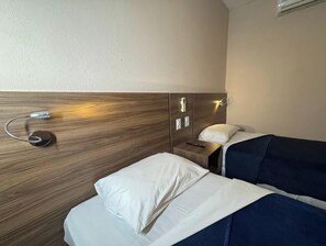 Een hotelkamer met twee bedden, een nachtkastje, een lamp en een wandairconditioning.