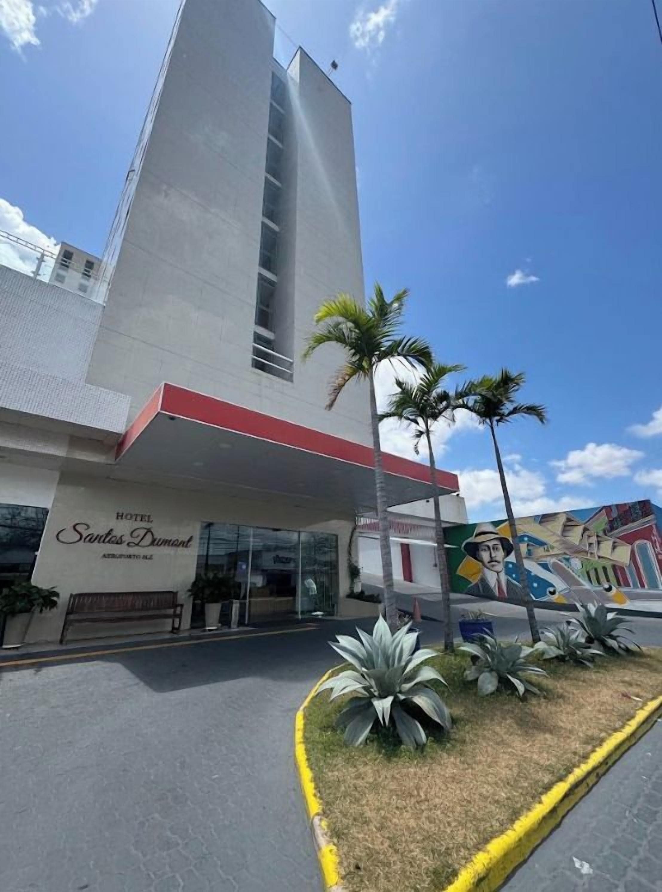 A hotel entrance with a modern design, a covered waiting area, and a mural on the wall.