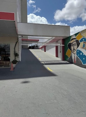 An outdoor corridor with a covered walkway, a mural, and a building entrance. - Hotel Santos Dumont Aeroporto SLZ (São Luís)