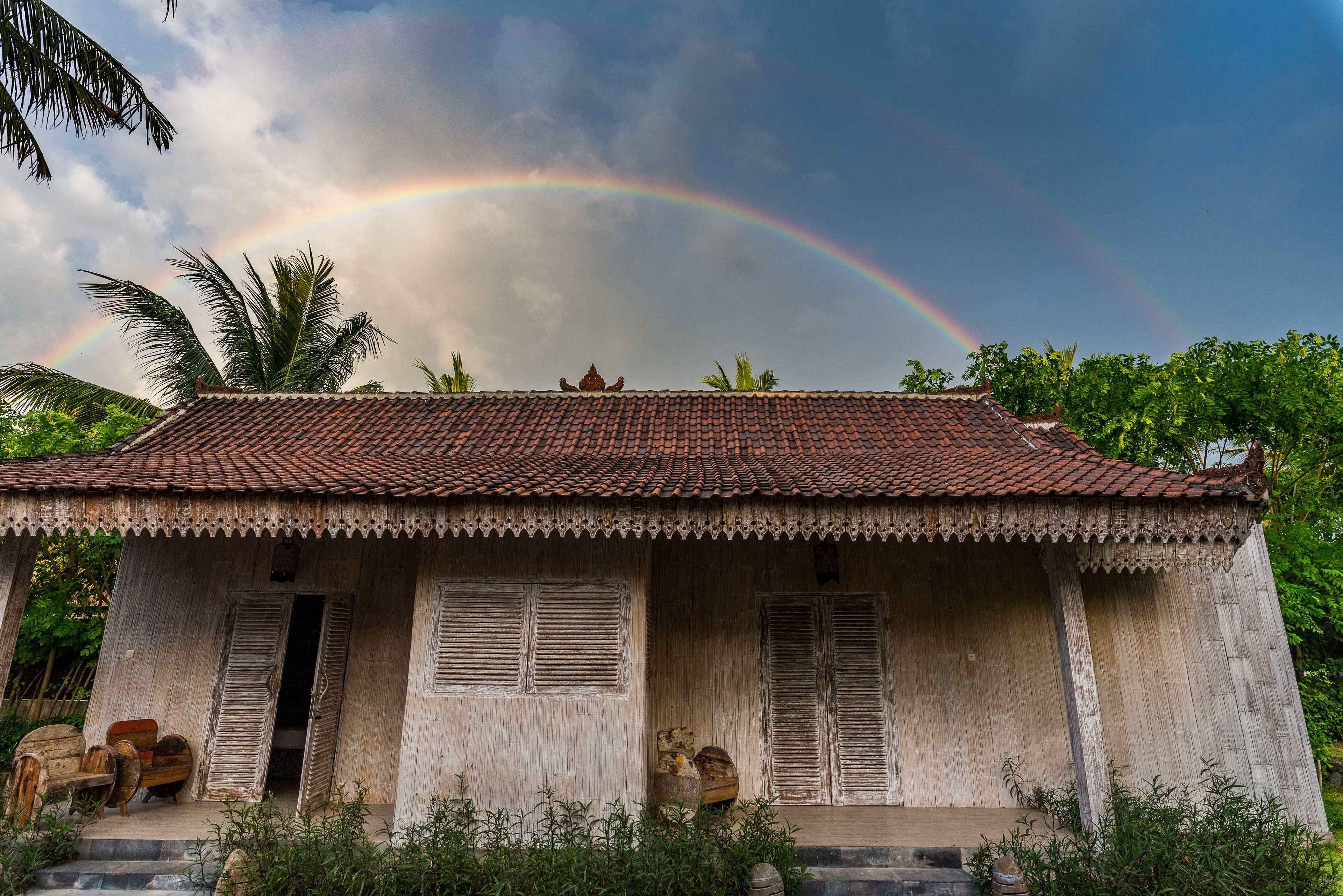 A rustic wooden house with a tiled roof, a porch, and a small shrine.