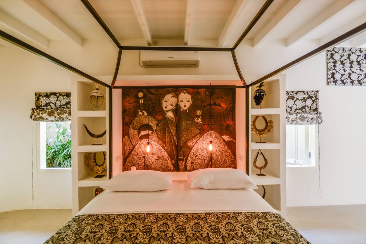 A bedroom with a large bed, a decorative wall with artwork, and shelves with various items.