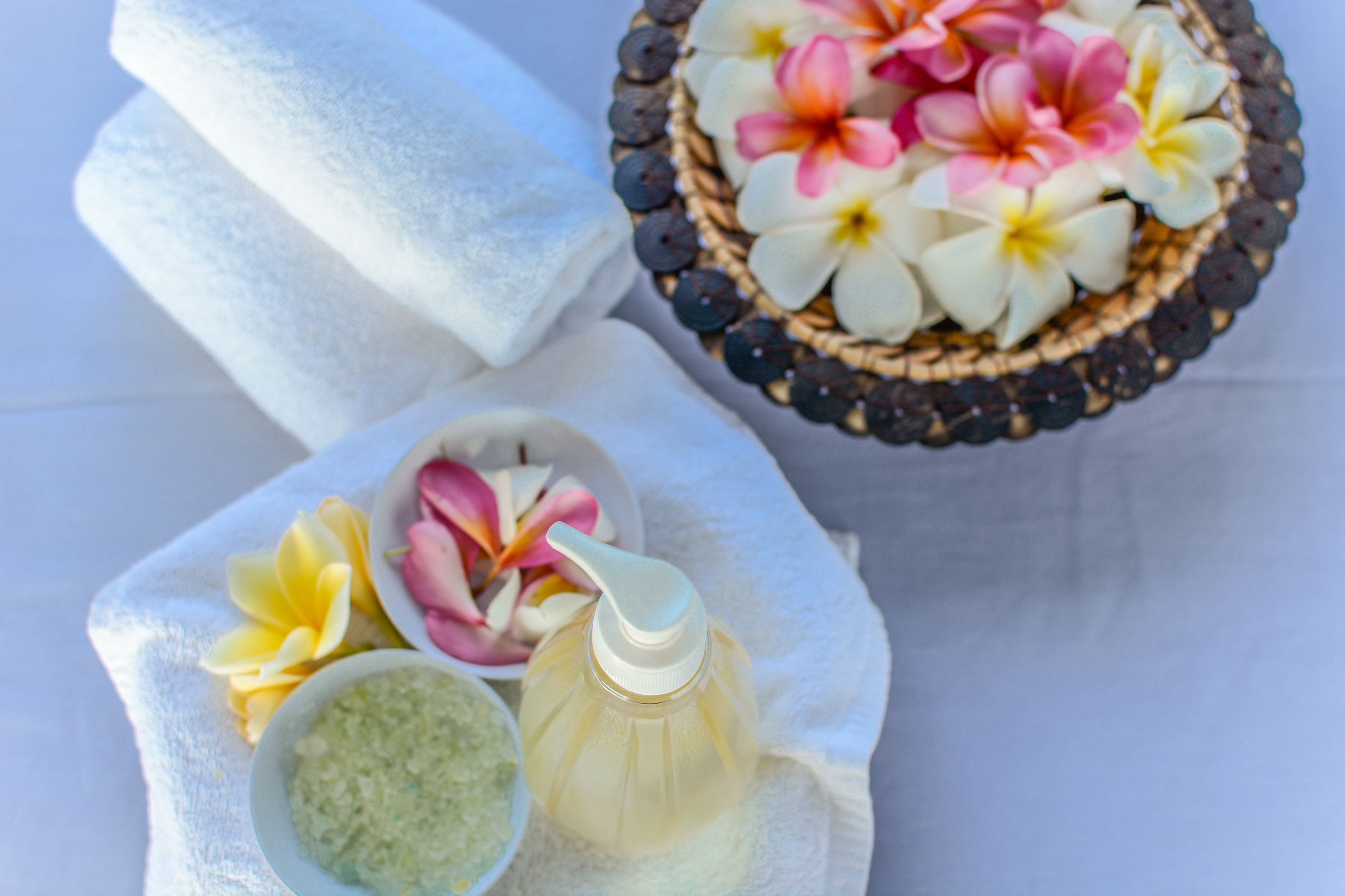 A spa setting with towels, a bowl of flowers, and a bottle of liquid.