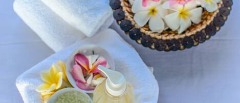 A spa setting with towels, a bowl of flowers, and a bottle of liquid.