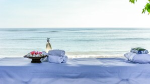 Un spa frente a la playa con una cama, toallas, un difusor y un arreglo floral.
