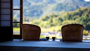 Een kamer met twee rieten stoelen en twee kleine bekertjes op een tafel, met uitzicht op bergen door een raam.