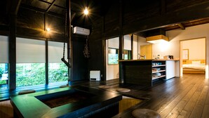 Een modern interieur met een houten vloer, een centraal geplaatst wastafelmeubel en een klein keukenhoekje met een koelkast en planken.