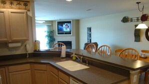 A kitchen with wooden cabinets, a dishwasher, and a sink. There is a dining area with chairs and a table. A television is mounted on the wall. - Condo 331 Parkview Bay, Osage Beach Super Nice Lakefront Condo (Osage Beach)