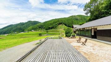 A wooden deck with a view of a lush green valley and a building with large windows.