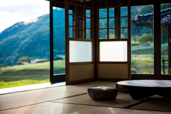 A tatami mat room with a view of a mountainous landscape through a shoji screen.