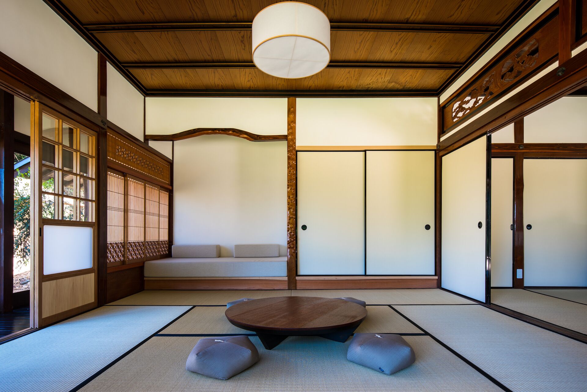A traditional Japanese room with tatami flooring, a low wooden table, cushions, sliding doors, and a hanging light fixture.