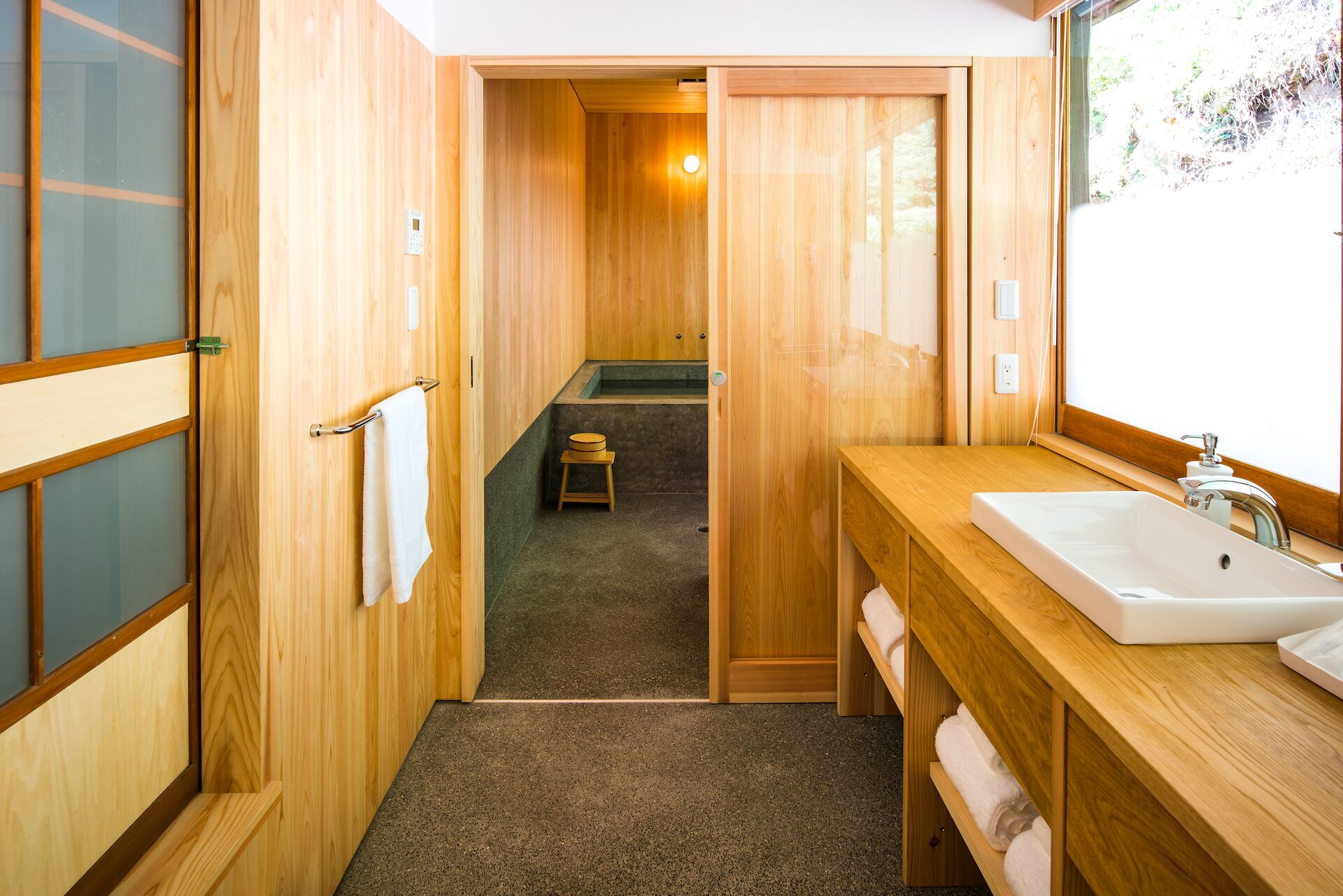 A wooden interior with a sink, towel rack, and a small stool.
