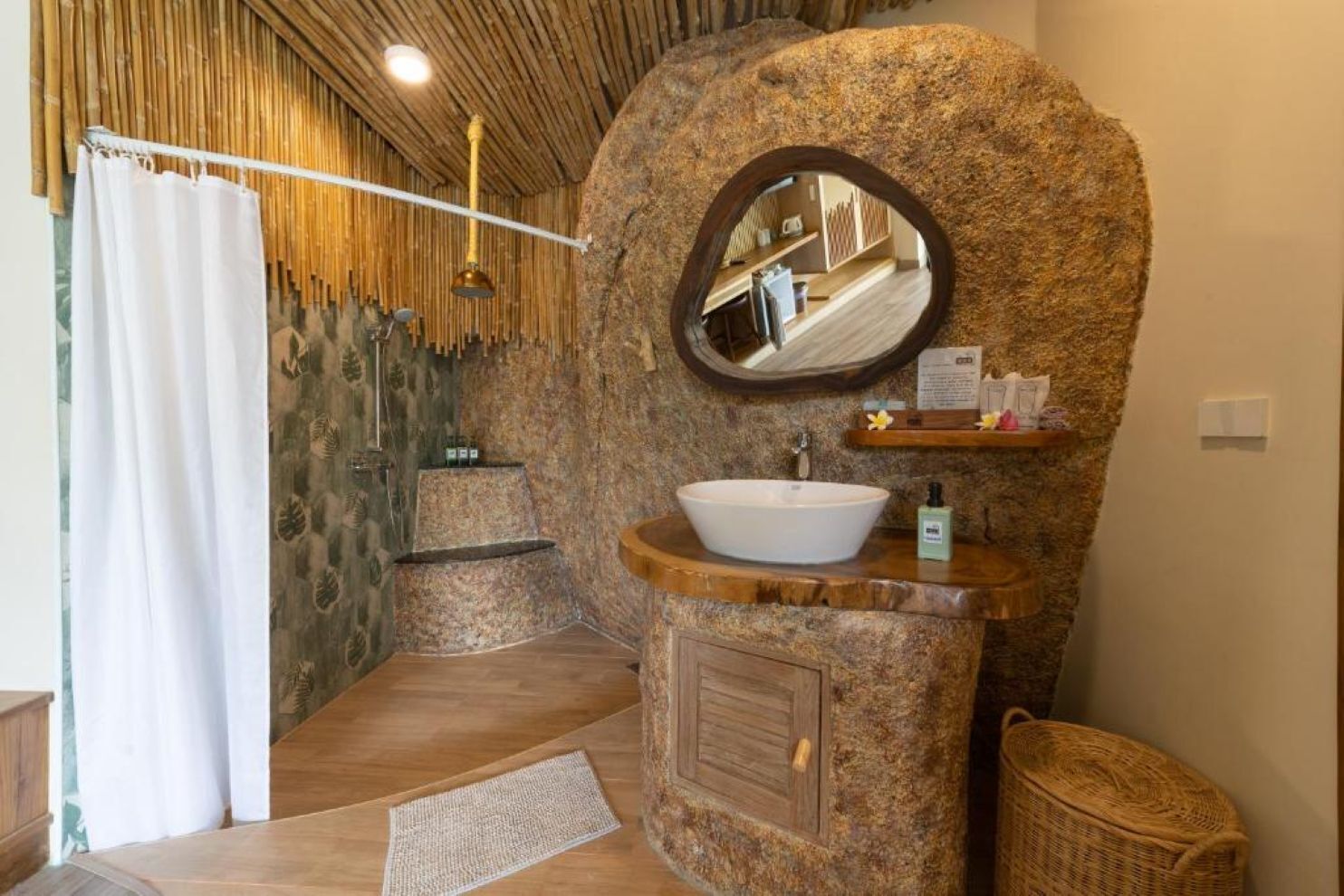A bathroom with a stone sink, a mirror, and a shower area with a bamboo curtain.