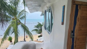 Eine Treppe führt zu einem Strand mit Blick auf den Ozean, einer Palme und einer Holztür mit blauem Streifen.