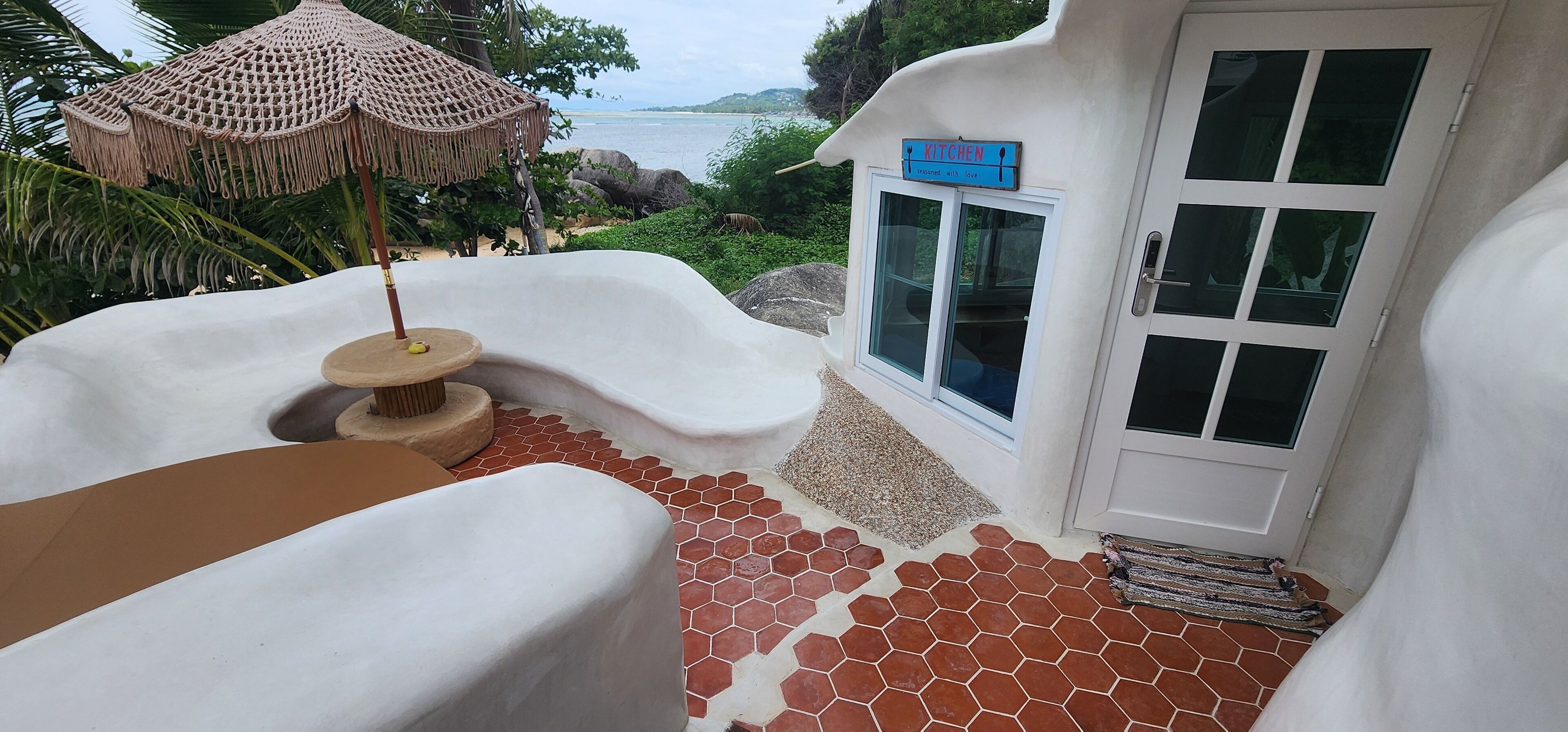 Un espacio cubierto con mesas y vistas al mar, un letrero de cocina y piso de baldosas.