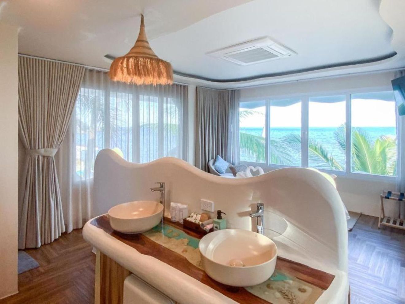 Un baño moderno con un diseño curvo único, que incluye dos lavamanos grandes de color blanco y una encimera de madera.