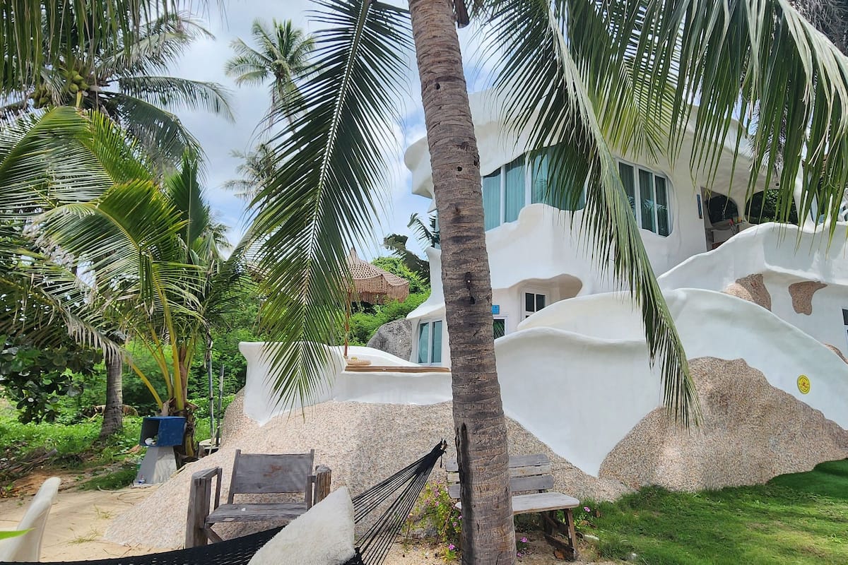 Un complexe hôtelier doté d’un bâtiment moderne de couleur blanche, de palmiers et d’un hamac.