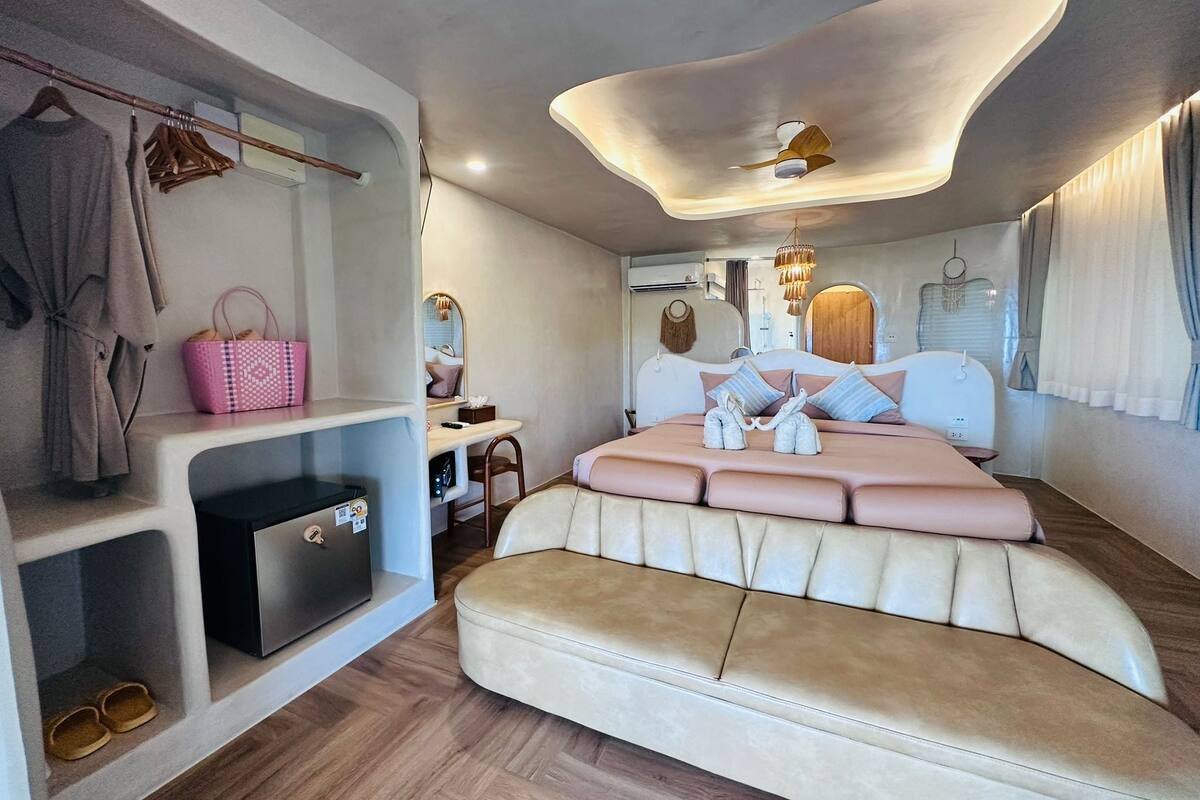 Une chambre à coucher moderne avec un plafond incurvé, un lit doté d’une tête de lit capitonnée, une coiffeuse avec un miroir et une étagère où sont posées des chaussures et un sac à main.