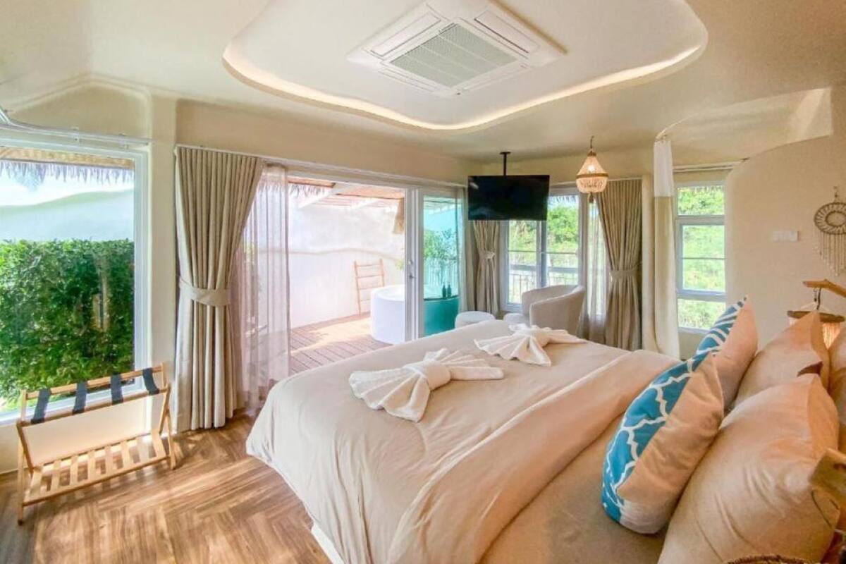 Une chambre spacieuse avec un grand lit, une télévision et une vue sur la verdure environnante.