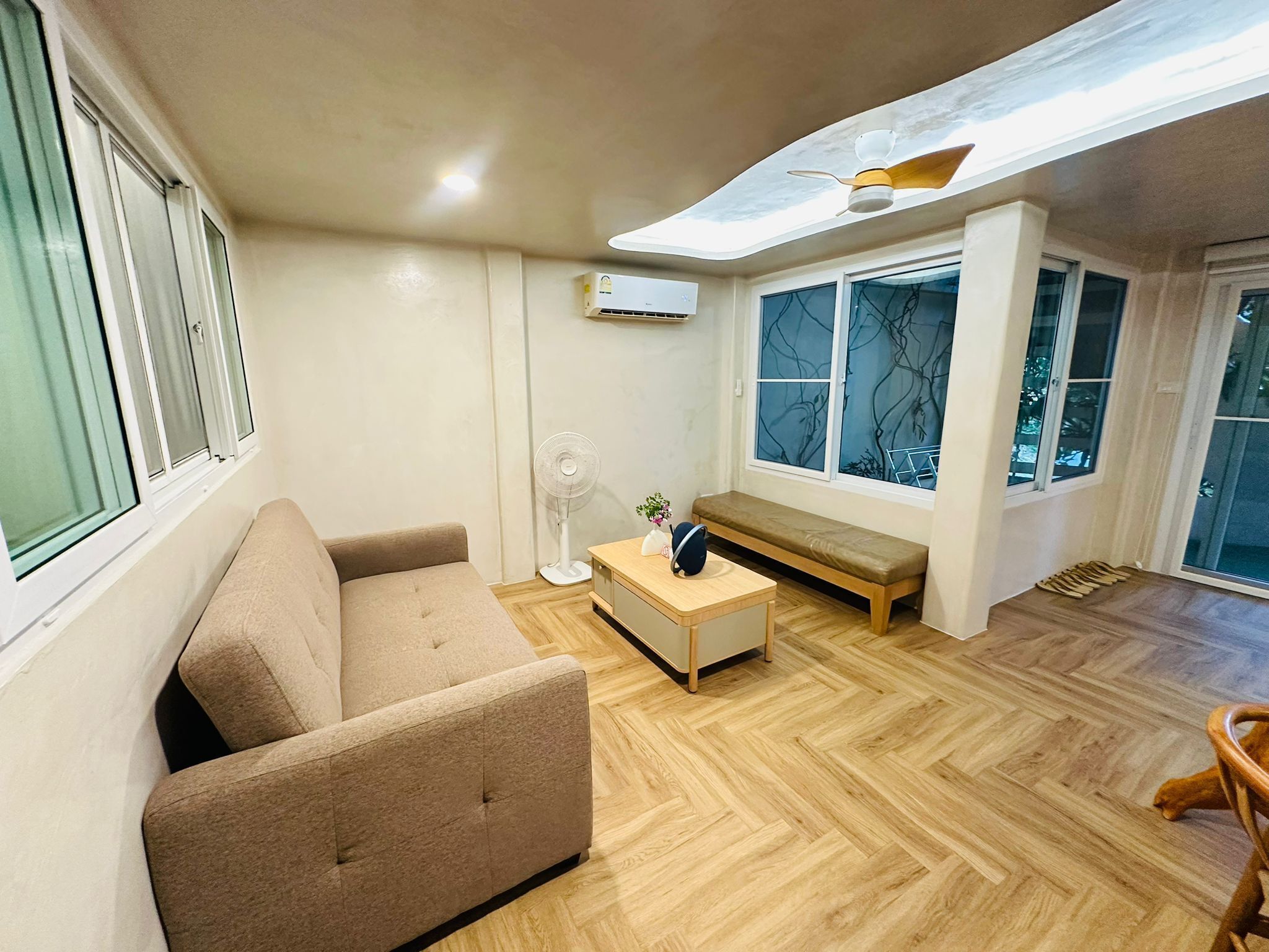A modern living room with a sofa, a wooden coffee table, a bench, and a ceiling fan.