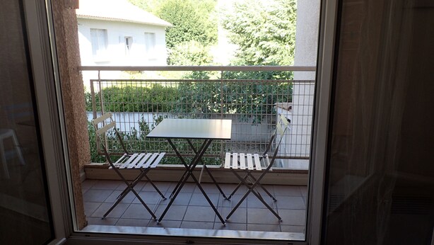 A balcony with a metal railing, a table, and two chairs.
