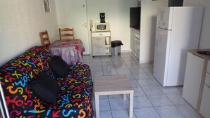 A compact living space with a sofa, a small table, a microwave, a refrigerator, and a kitchenette area.