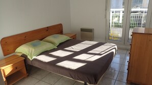 A bedroom with a wooden bed, two nightstands, a wooden dresser, and a sliding glass door to a balcony.