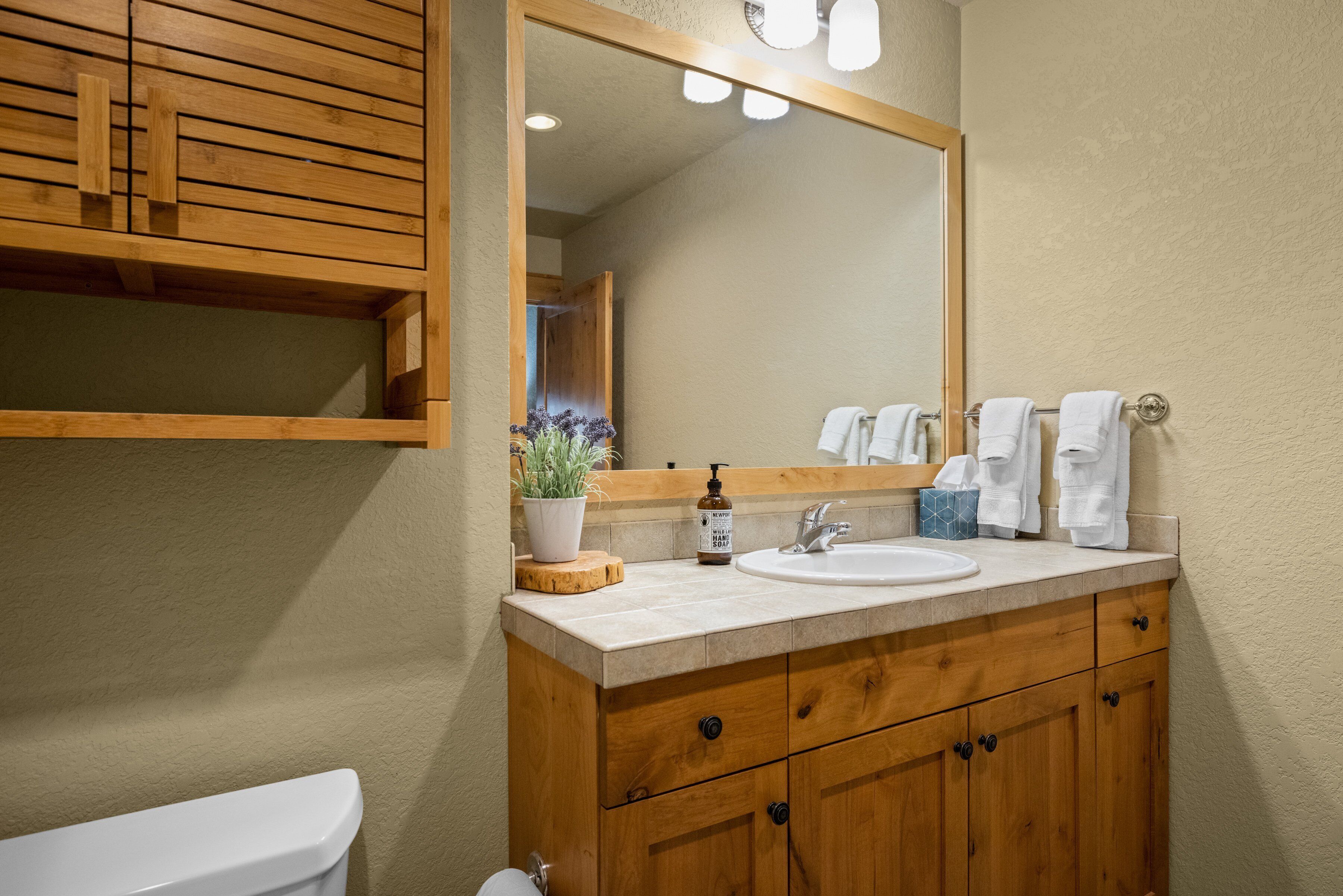 A bathroom with a wooden vanity, a sink, a mirror, and a toilet.