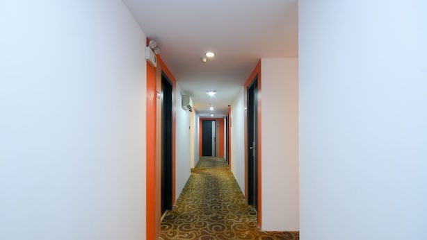 A hotel hallway with patterned carpet, orange accents on the walls, and a ceiling light. - Hotel O agon Inn (Miri)