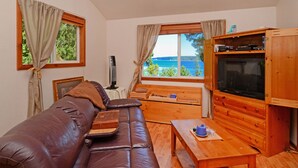 Un salon chaleureux avec un canapé en cuir, une table en bois et un téléviseur. Il y a des fenêtres avec des rideaux, et on peut admirer la vue sur la mer.