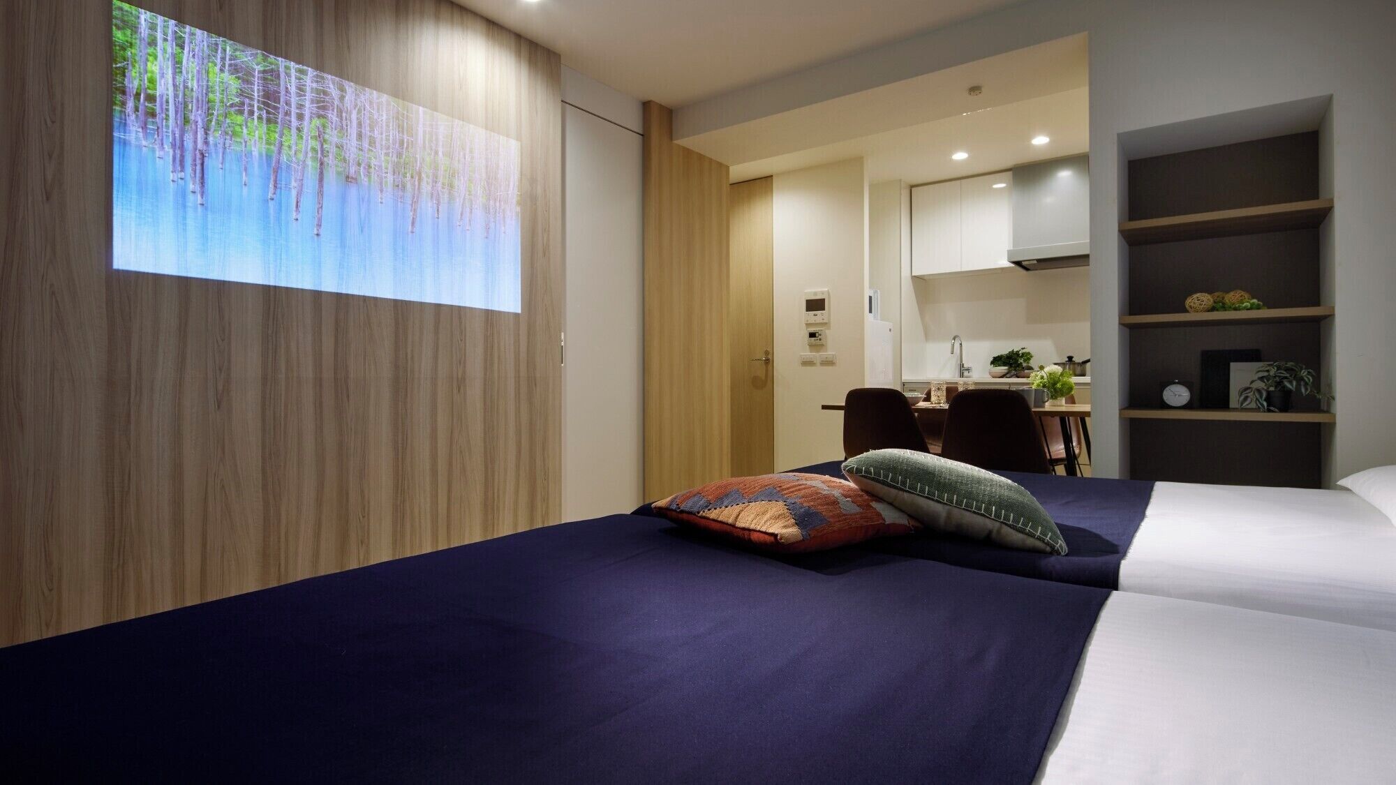 A modern hotel room with a large bed, a desk, and a kitchen area.