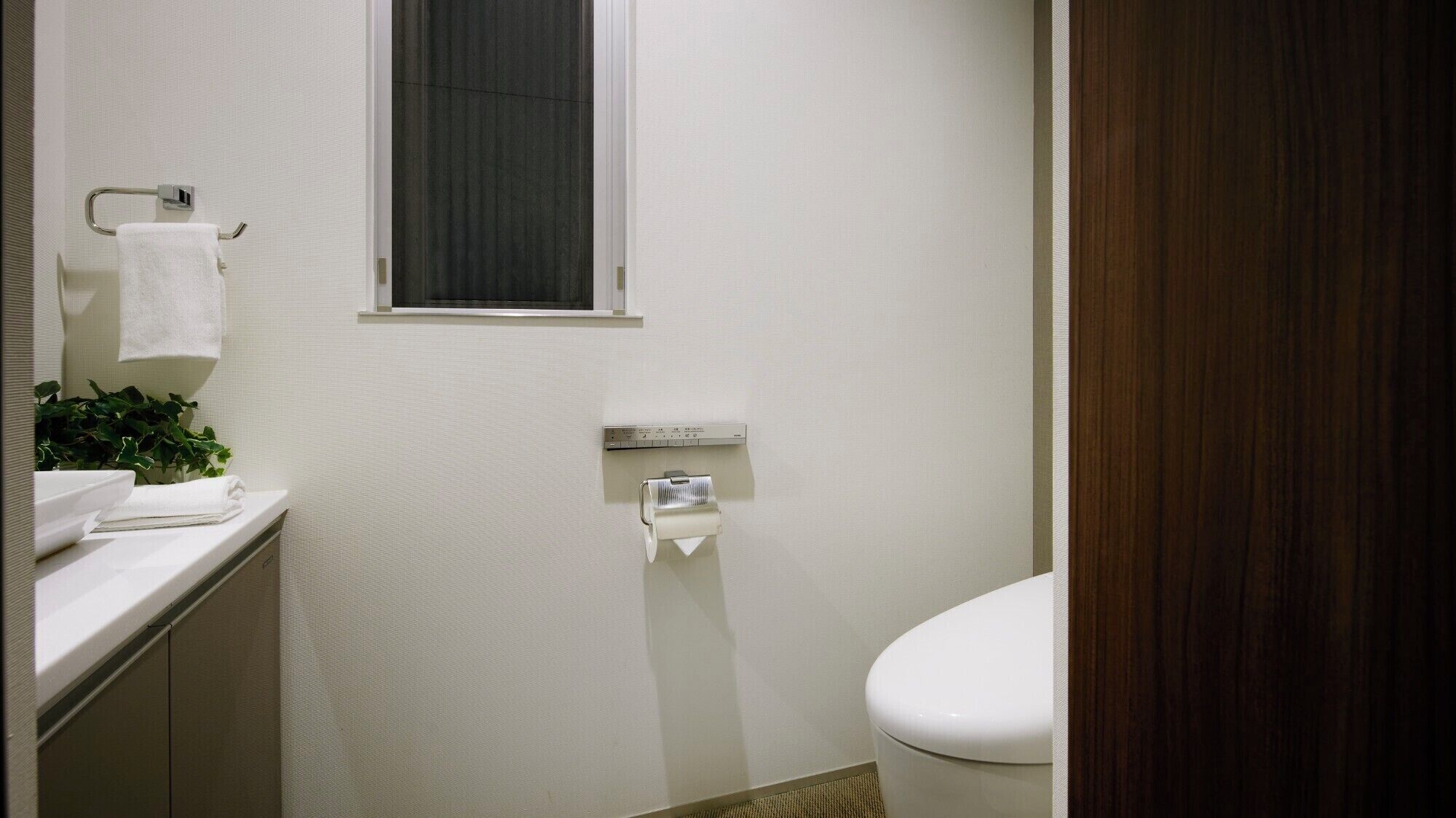 Ein Badezimmer mit Toilette, Handtuchhalter, einem Fenster und einem Papierhandtuchspender.