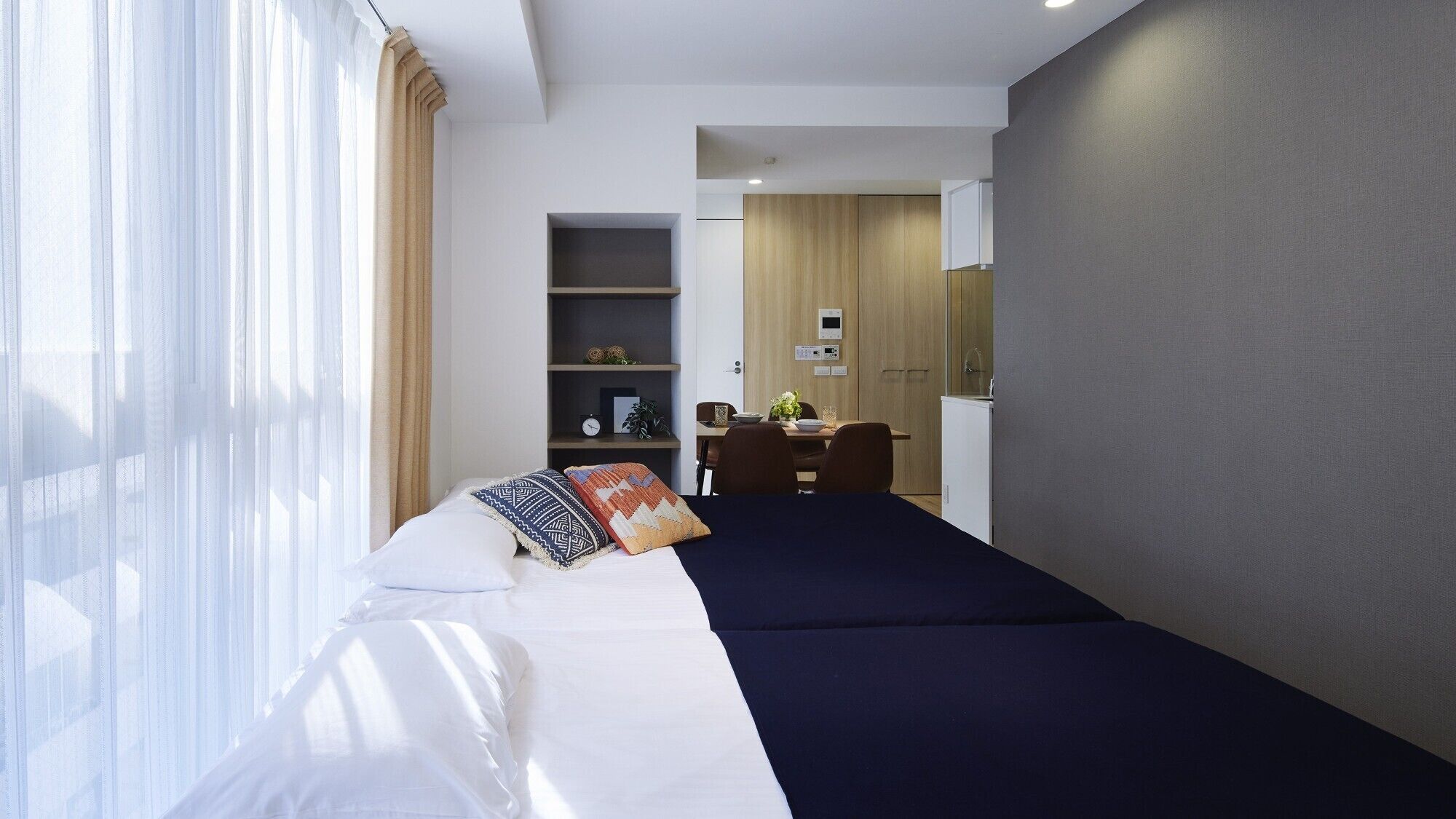 A hotel room with a bed, a desk, a wardrobe, and a small kitchenette.