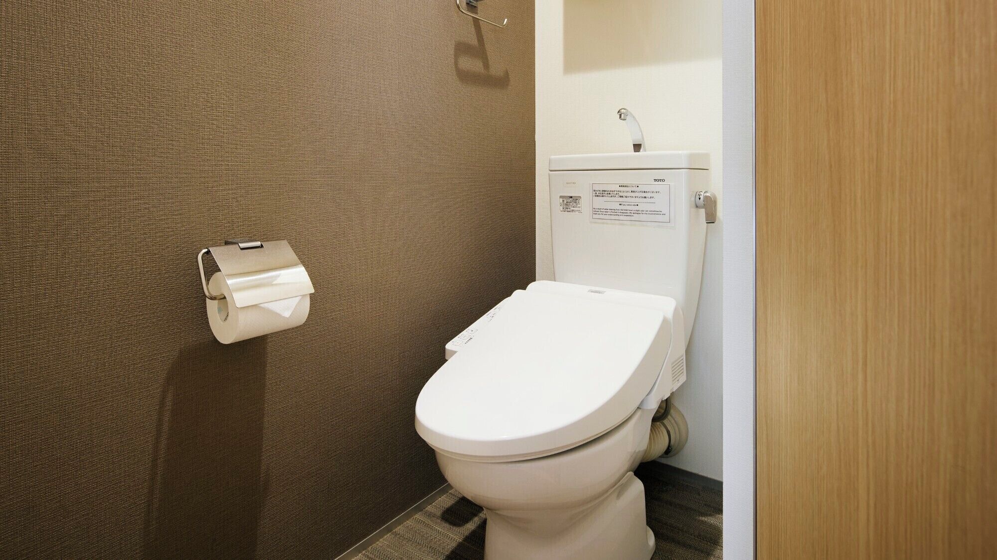 A bathroom with a toilet, a paper towel dispenser, and a toilet paper roll.