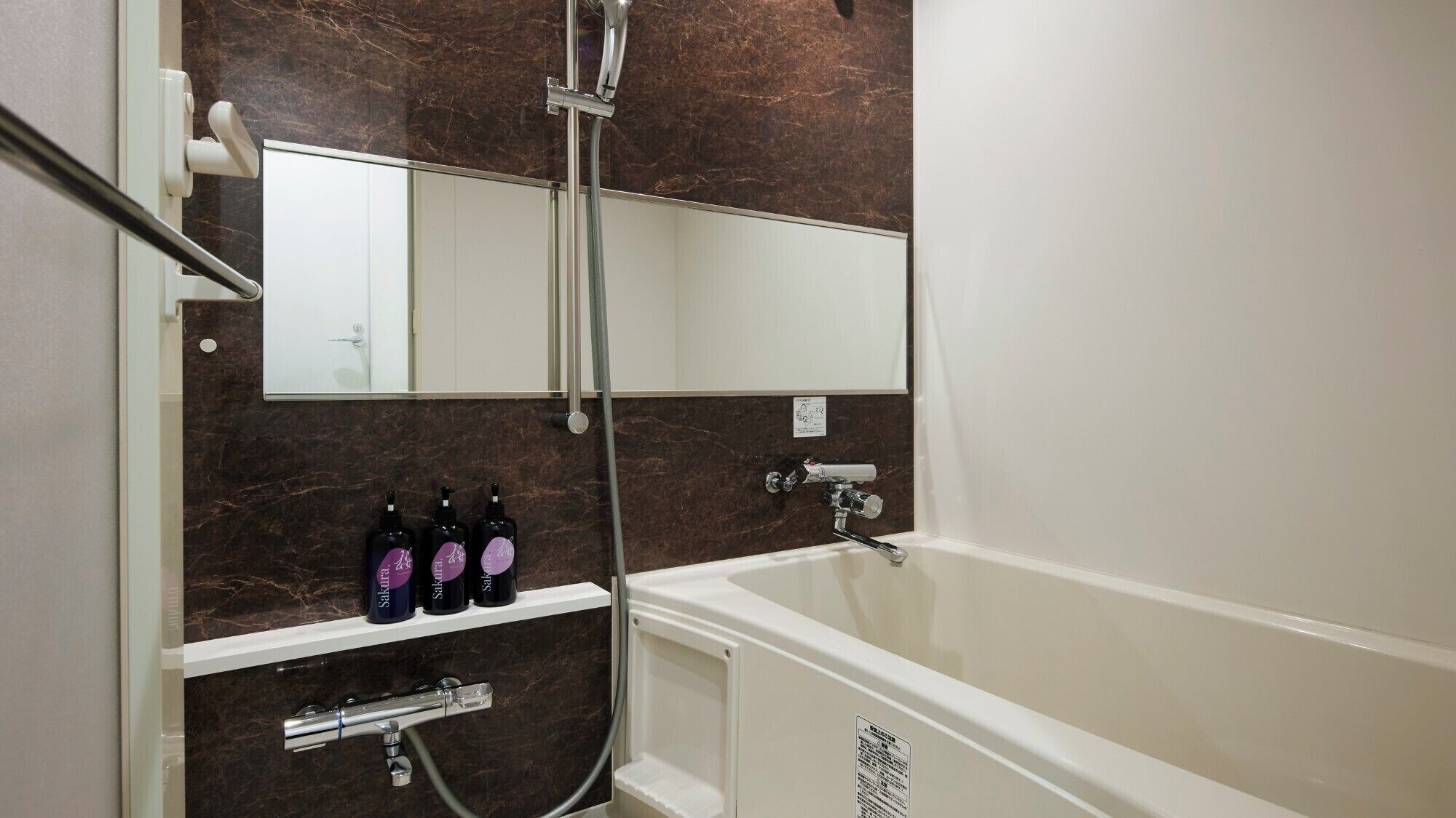 A bathroom with a bathtub, a shower, and a mirror. There are three bottles on a shelf.