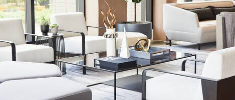 A modern living room with a glass coffee table, white sofas, and a potted plant.