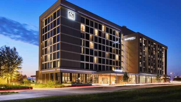 A modern hotel with a glass facade, multiple floors, and a well-lit entrance. - AC Hotel by Marriott Dallas Frisco (Frisco)