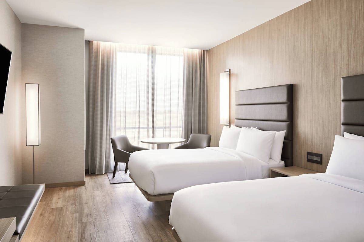 A hotel room with two beds, a desk, a chair, a TV, and a window with curtains.