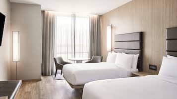 Une chambre d’hôtel avec deux lits, un bureau, une chaise, une télévision et une fenêtre avec des rideaux.