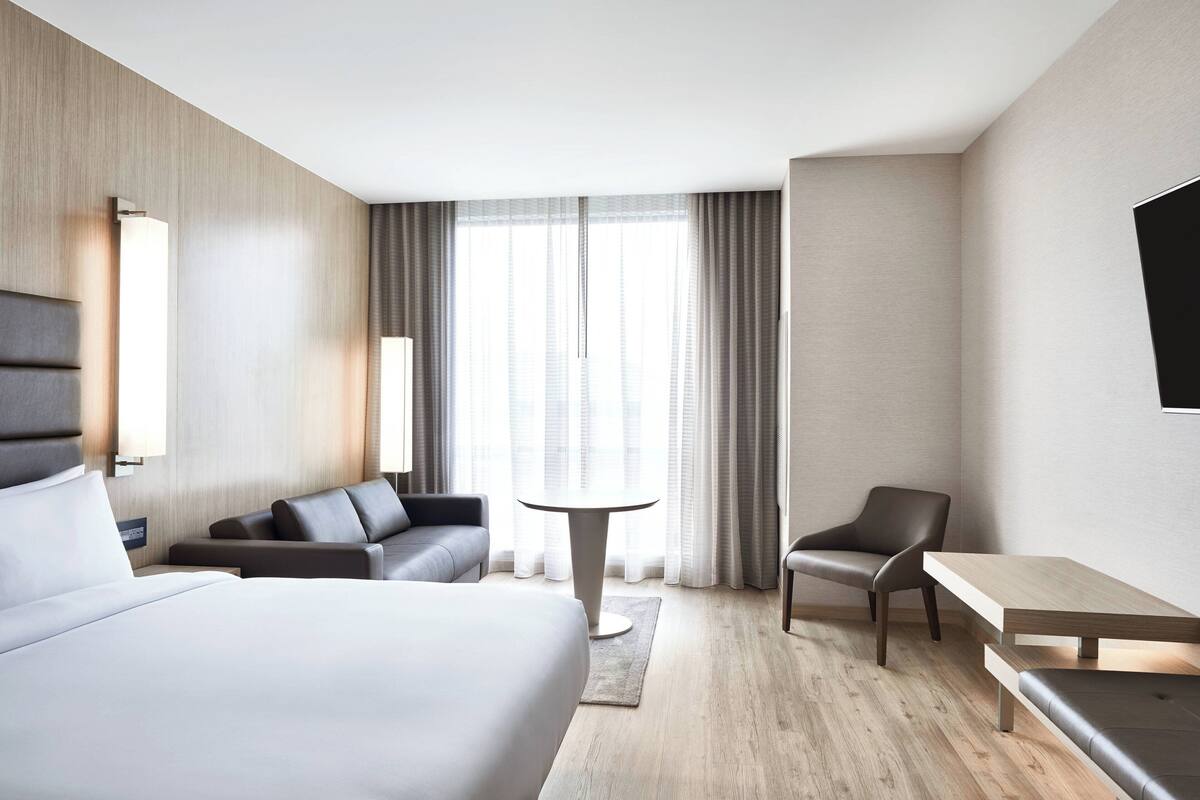 A modern hotel room with a large bed, a sofa, a small table, and a TV mounted on the wall.