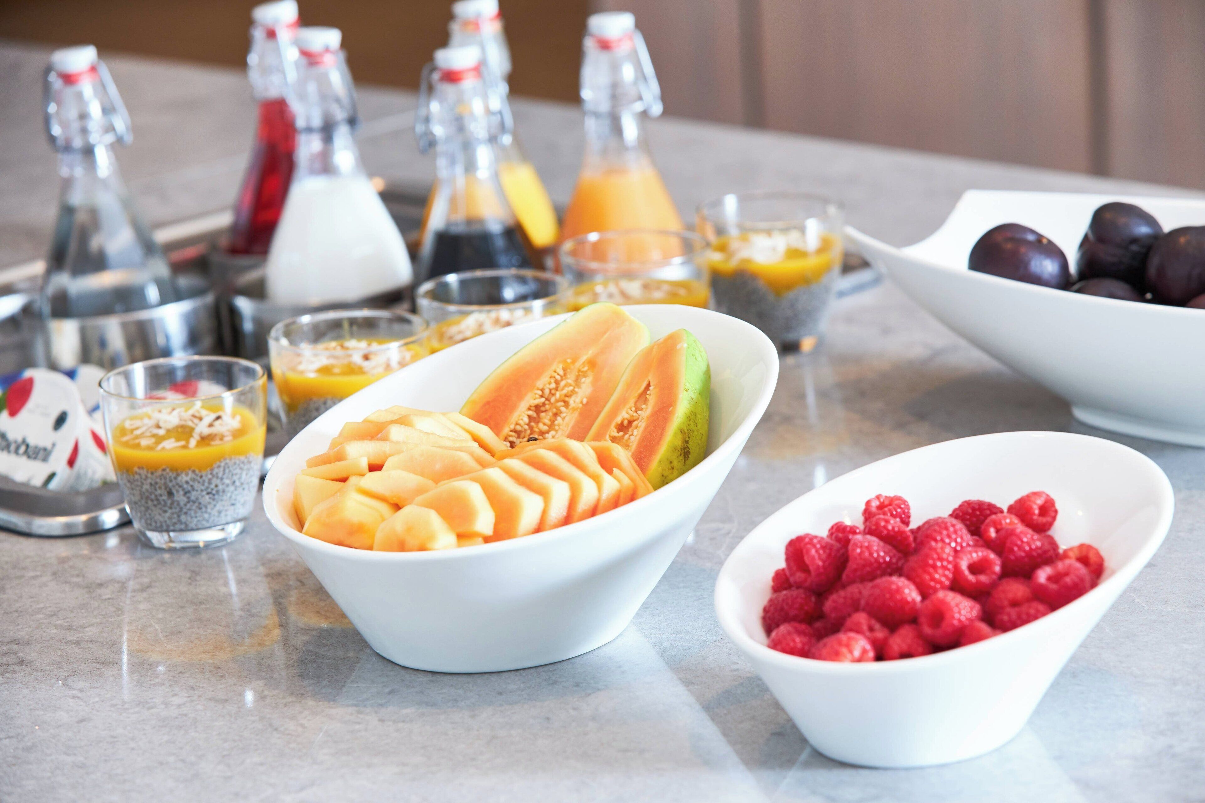 A table with bowls of sliced fruits and various beverages.