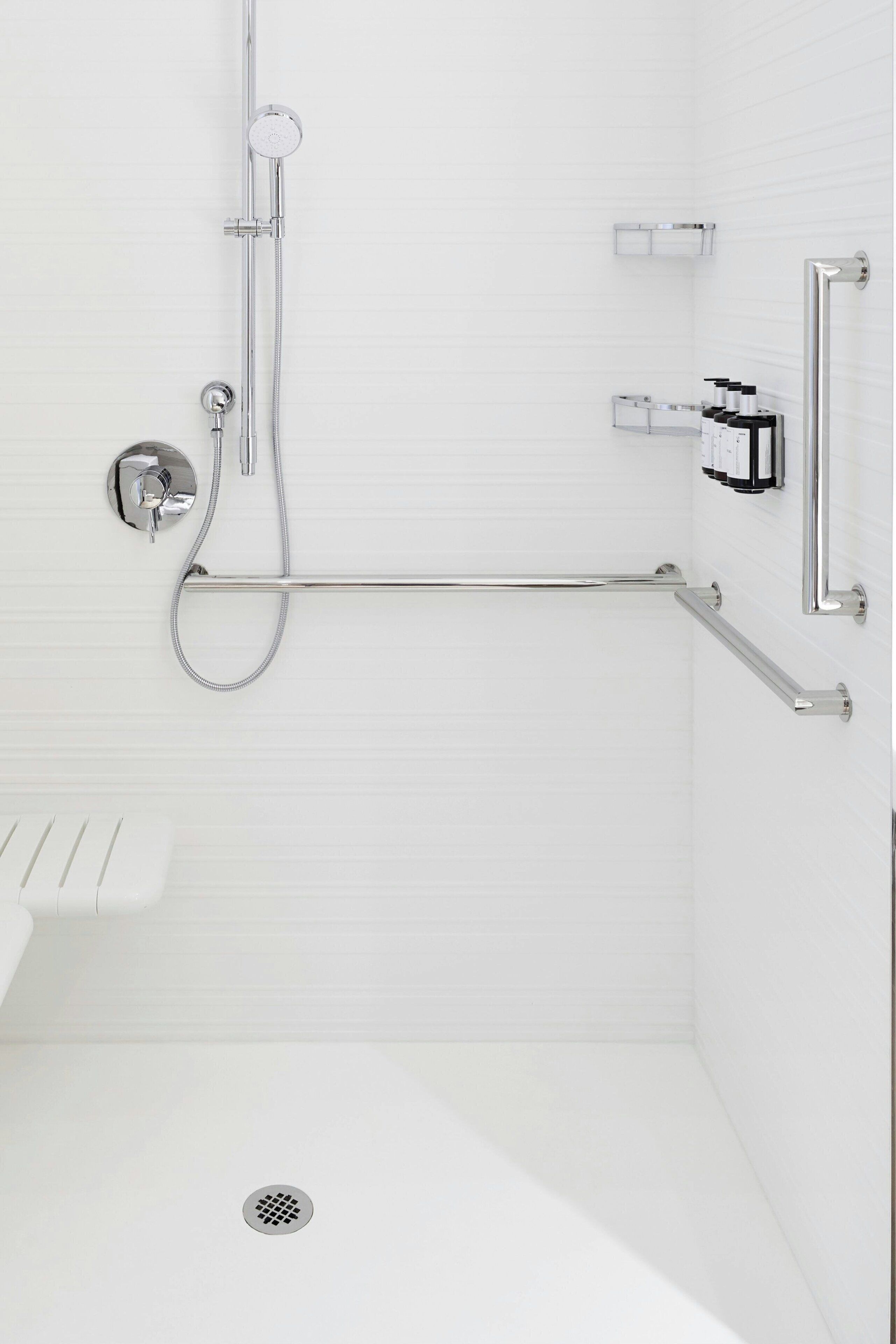 Ein modernes Badezimmer mit bodengleicher Dusche, Haltegriffen und Toilette mit Sicherheitskissen.