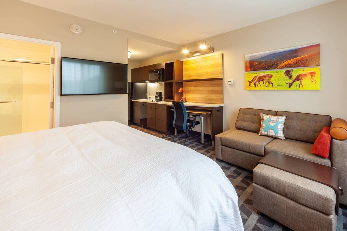 A hotel room with a large bed, a desk with a chair, a sofa, a TV, and a painting on the wall.