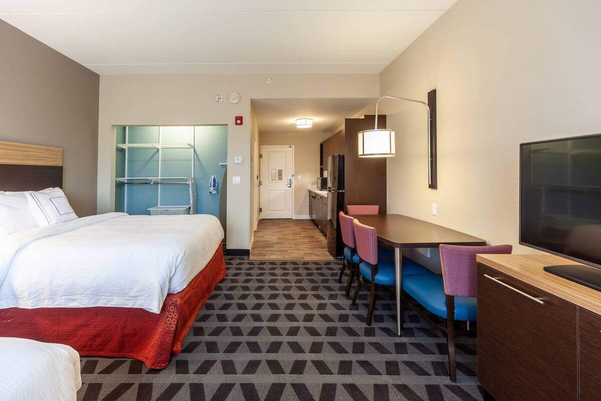 A hotel room with a bed, a desk with a chair, a television, and a kitchenette.