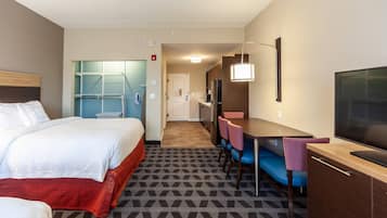 A hotel room with a bed, a desk with a chair, a television, and a kitchenette.