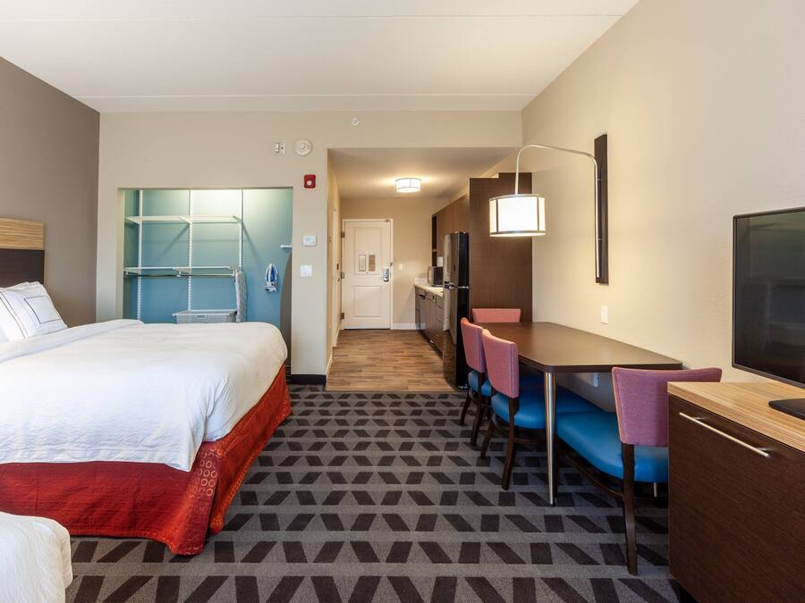 A hotel room with a bed, a desk with a chair, a television, and a kitchenette.