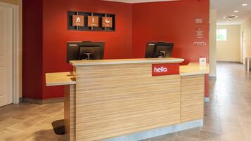 A reception desk with a 'hello' sign, two Lenovo computers, and a red wall with icons for 'Stay', 'Work', and 'Play'.