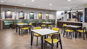 Un restaurante moderno con asientos verdes, sillas amarillas y mesas de madera.